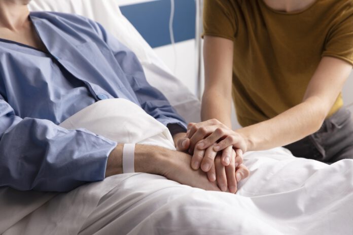 wife-visiting-her-ill-husband-scaled-hand-holding-on-hospital-bed-with-IV-drip-in-background